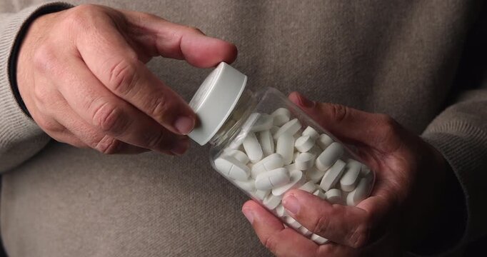 Person opening a transparent medicine bottle and taking out pills for daily treatment at home representing healthcare and wellness.