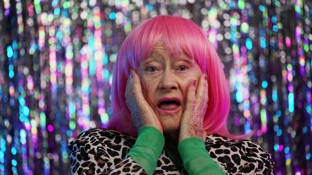 Portrait of eccentric pink-haired senior woman expressing wonder, wow gesture