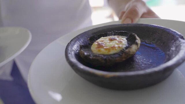 Waiter presenting baked mushroom with melted kashar cheese in clay pot