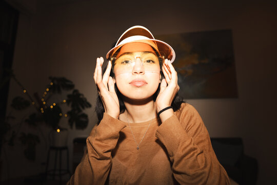 A young woman wearing a visor and glasses adjusts her headwear, looking directly at the camera with a neutral expression.
