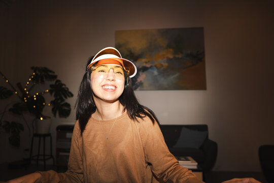 A young woman wearing a visor and glasses smiles warmly while indoors.