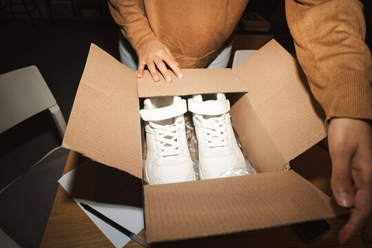 A person opens a cardboard box revealing a pair of new white sneakers.
