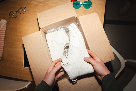A person is unboxing a new pair of white high-top sneakers from a cardboard package.