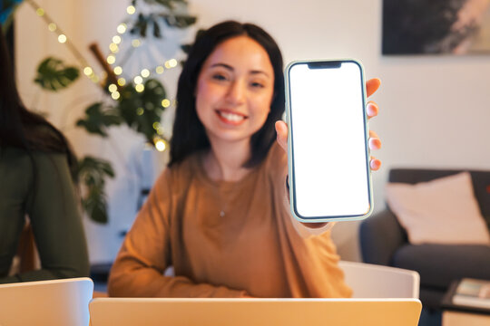 A smiling woman holds up a smartphone with a blank screen, inviting viewers to imagine its content.
