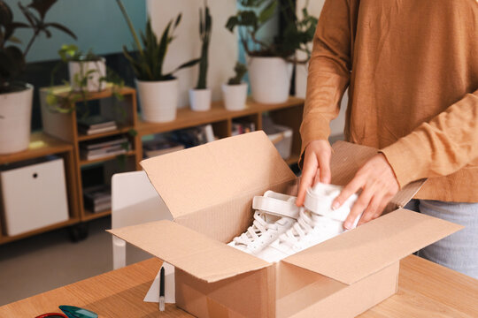 A person is unboxing a new pair of white high-top sneakers from a cardboard package.