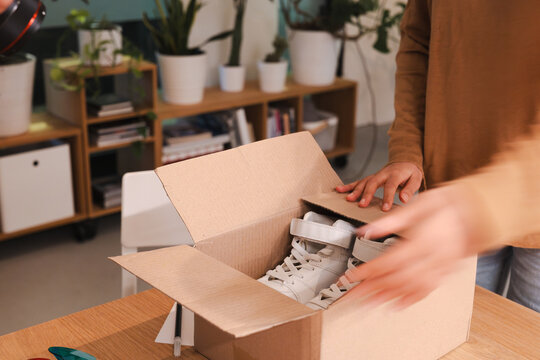A person opens a cardboard box containing a pair of white sneakers, revealing a new purchase.