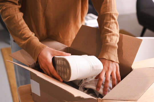 A person is unboxing a new pair of white shoes from a cardboard package.
