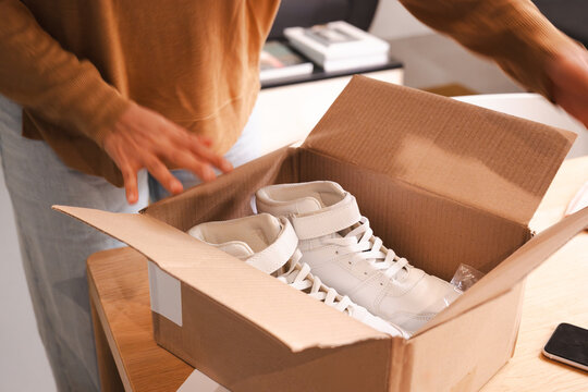 A person opens a cardboard box to reveal a new pair of white high-top sneakers.