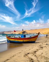 Obraz premium A vibrant, colorful boat rests on a sandy beach under a partly cloudy, bright blue sky with hills in the background