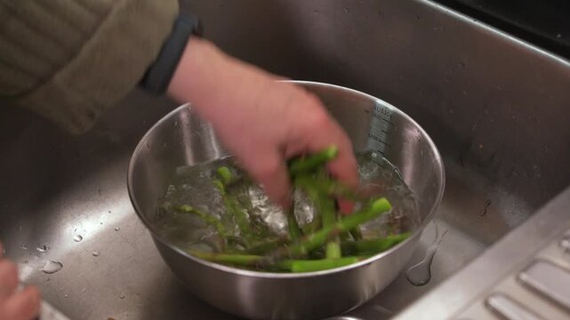 Person washing fresh green asparagus in a bowl of water
