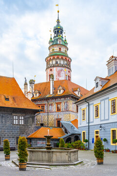 The photo shows a castle tower in Cesky Krumlov. It is a summer day, and people visit the historic town. The architecture reflects the unique style of the area.