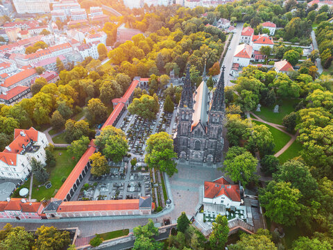Vysehrad Basilica of St. Peter and St. Paul rises majestically amid lush greenery during a golden sunrise in Prague, showcasing Gothic architecture and serene surroundings.