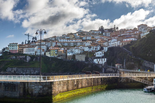 Vista panor&aacute;mica del puerto y pueblo de Lastres en Asturias, con su muelle de piedra y farola tradicional frente a casas escalonadas en la colina, Espa&ntilde;a.