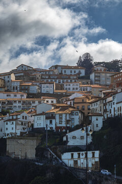 Vista vertical del pintoresco pueblo costero de Lastres en Asturias, Espa&ntilde;a, con sus tradicionales casas blancas y tejados de terracota apilados en la ladera de una colina empinada sobre el mar.