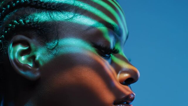 Artistic portrait with colorful light patterns. Model poses against blue background. Vibrant colors enhance facial features and create dynamic atmosphere. Innovative visual art experience.