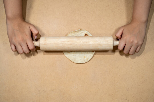 Hands using rolling pin to flatten dough on kitchen surface