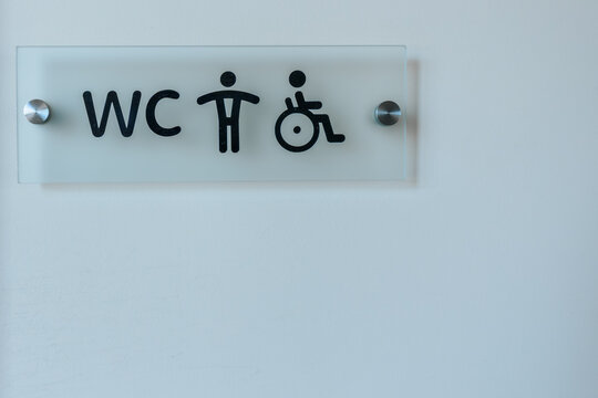 Signage indicating restroom facilities with symbols for male, female, and accessible options displayed on a frosted glass panel mounted on a wall