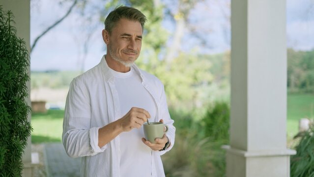 Happy man drinking coffee on porch of countryside home. Satisfied businessman starting business day with smile and confidence before going to work. Successful entrepreneur on terrace of ranch house.