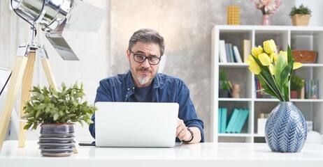 Bearded man working online with laptop computer at home sitting at desk. Home office, browsing...