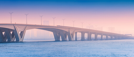 bridge providing a modern architectural link over calm water during an atmospheric morning in Abu Dhabi. Urban silhouettes visible in the distance © EdNurg