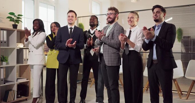 Diverse business team in office giving applause. Colleagues stand together after a meeting, celebrating success. Bright workplace where people feel achievement and unity. Strong teamwork theme.