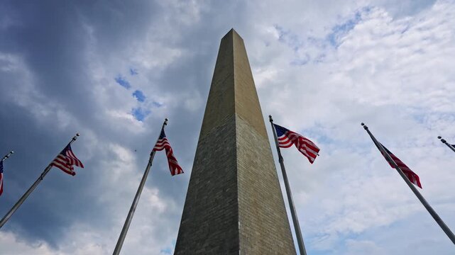 American flags surrounding historic Washington Monument. National memorial representing United States history. Patriotic architecture in Washington DC. Iconic obelisk with waving American flag.