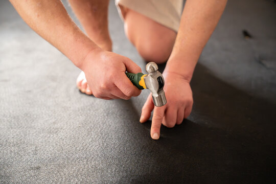 Man accidentally hitting his finger with hammer while fixing flooring underlay during home renovation showing painful hand injury and unsafe work situation