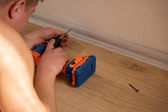 Man installing plastic floor skirting board using cordless screwdriver on linoleum flooring during home renovation and interior finishing work