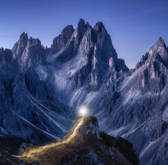 Fototapeta premium Flashlight trails on mountain path against high rocks at night in autumn. Tre cime, Dolomites, Italy. Colorful landscape with light trails, trail on the hill, mountain peaks, sky with stars in fall
