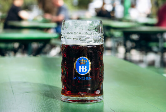 Munich, Germany - April 15, 2025: Glass mug of dark Hofbrau Munchen beer on a table in a traditional beer garden in Munich, Germany