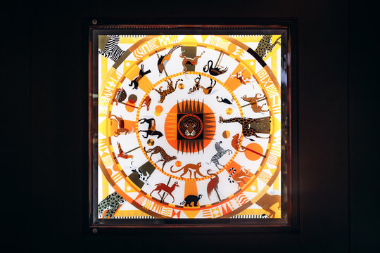 Munich, Germany - April 15, 2025: Herm&egrave;s silk scarf displayed in boutique window at Munich Airport, featuring colorful circular animal motif design in illuminated showcase