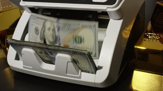 Counting hundred dollars bills with gold bars nearby. Cash counting machine with US dollars. Finance concept with dollars money and gold. Gold and cash dollars. Money counting process.