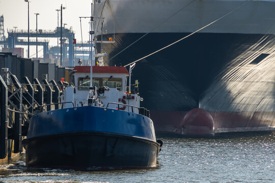 Blue service boat moored along a concrete pier in an Klaipeda industrial harbor, framed by dock fenders and stacked cargo containers, conveying maritime work, transport and port logistics on a sunny d