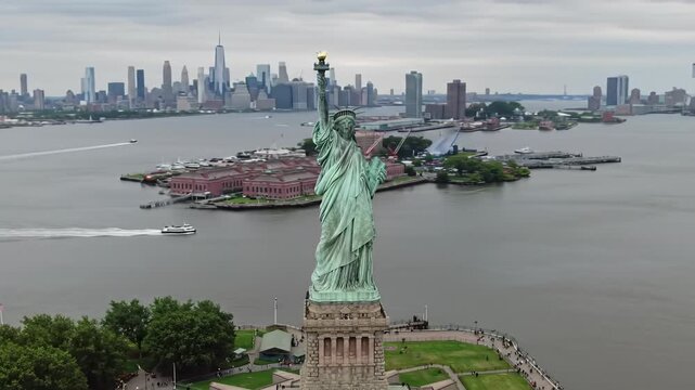 Majestic high-angle drone video slowly panning left across New York Harbor with Statue of Liberty, Ellis Island, and NYC/Jersey City skylines. American heritage concept