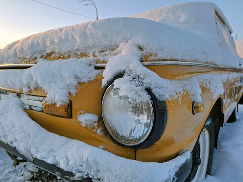 A yellow vintage car sits in the snow-covered parking lot