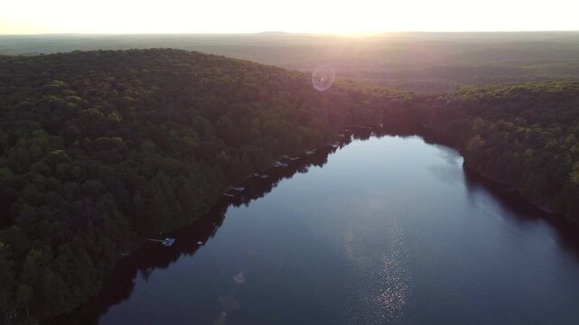 Aerial over Buckskin Lake into the sun with lens flare on a summer afternoon. Lakeside cottages and crown land wilderness in Tory Hill, Halliburton Highlands East, Ontario, Canada.