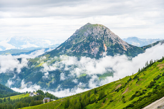Majestic mountains rise above the rolling clouds in the Low Tauern region of Austria. Lush green hills contrast with rocky peaks, offering a stunning view of nature's beauty.