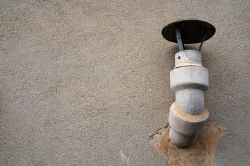 Asbestos cement flue pipe with cap protruding from stucco wall of building
