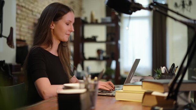 Woman working in home office with laptop computer, blogger writing online, browsing internet, concentrating, focusing, busy.