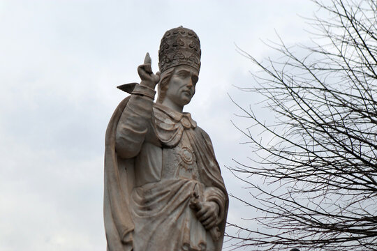 Statua in pietra di Papa Gregorio Magno con triregno in gesto di benedizione accanto a rami d'albero spogli sotto un cielo nuvoloso a San Gregorio da Sassola