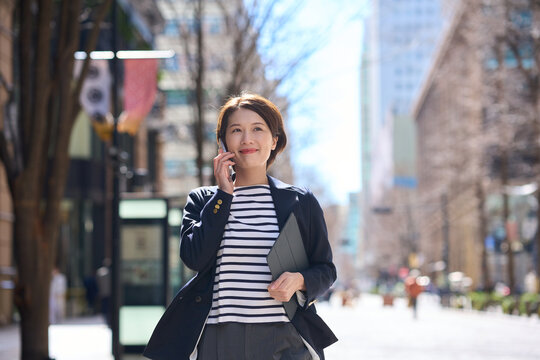 Businesswoman talking on smartphone while walking in the city street in spring