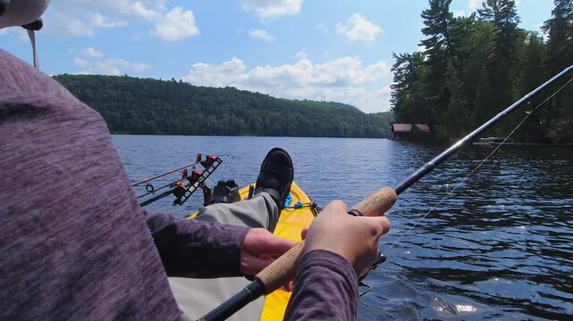 Kayak sport fishing at Lake Simcoe, Ontario. Adventure and tranquility. Angler glides across waters, surrounded by breathtaking shoreline views summer sky. Casting and reeling while enjoys solitude.