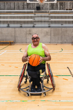 Smiling man with disability holding a basketball, participating in para sports for inclusion and determination in a gymnasium