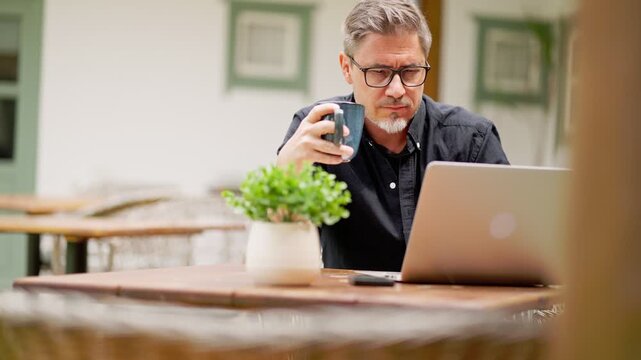 Casual middle age man sitting in garden working on laptop computer in home office. Businessman tele working