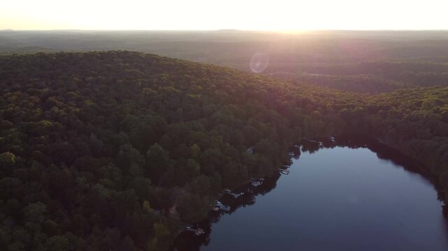 Aerial over Buckskin Lake into the sun with lens flare on a summer afternoon. above lakeside cottages along side crown land wilderness in Tory Hill, Halliburton Highlands East, Ontario, Canada.