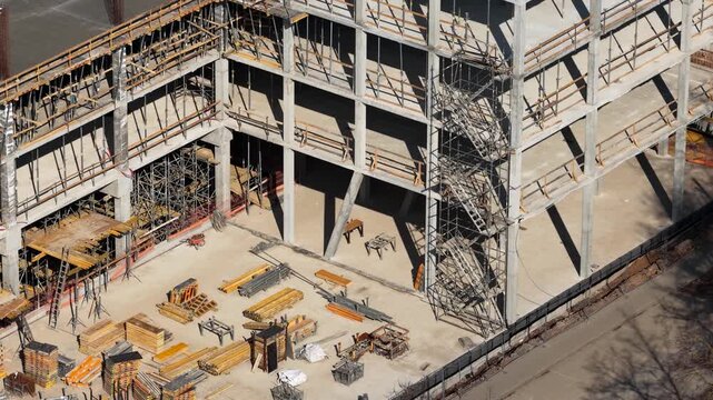 Drone shot of a multi-level concrete building frame with scaffolding, stairs, and organized construction materials on-site, highlighting structural development and engineering progress.