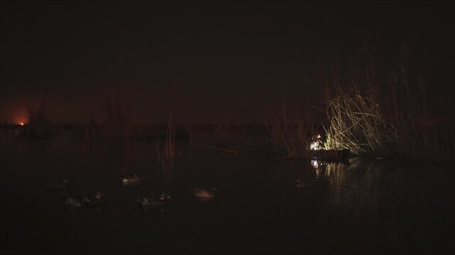 Hunter in a small boat using a spotlight to navigate a dark swamp with duck decoys floating nearby
