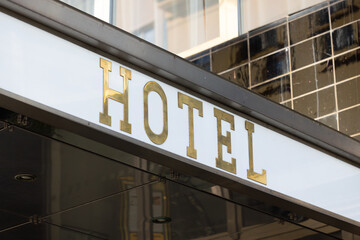 Fototapeta premium Hotel entrance sign with gold lettering against a modern glass facade, showcasing a contemporary architectural design in an urban setting