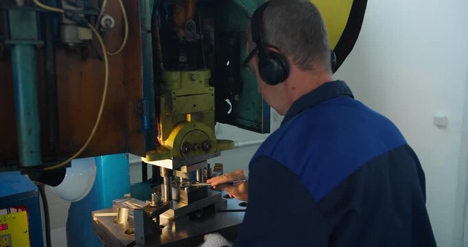 Blue collar worker at stamping press during metal forming operation. Industrial labor and factory manufacturing concept