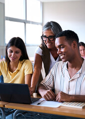 Vertical. A mature female educator assists a young man and woman during a computer lesson. They are...